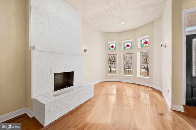 unfurnished living room with a brick fireplace, hardwood / wood-style floors, and a textured ceiling