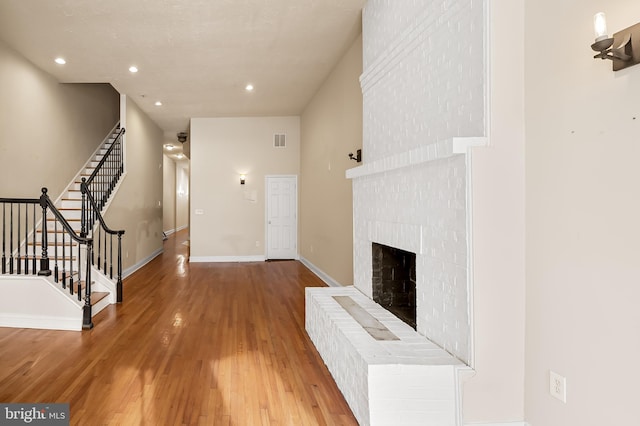 unfurnished living room featuring wood-type flooring and a brick fireplace