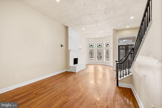 unfurnished living room with a brick fireplace, light hardwood / wood-style floors, and a textured ceiling