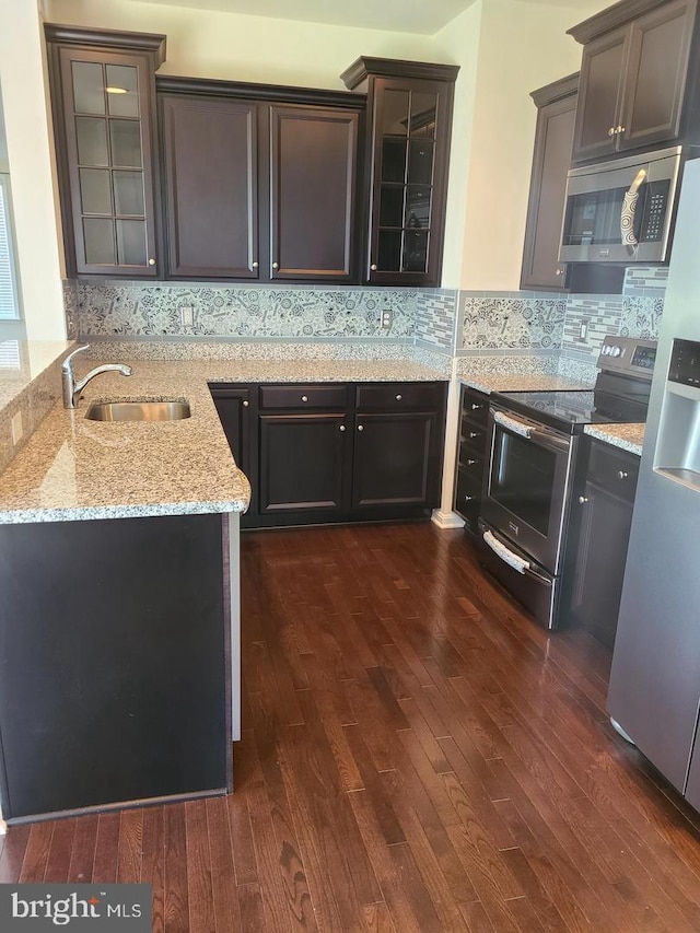 kitchen with stainless steel appliances, kitchen peninsula, light stone countertops, dark wood-type flooring, and sink