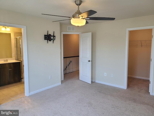 unfurnished bedroom with ensuite bathroom, ceiling fan, a closet, a walk in closet, and light colored carpet