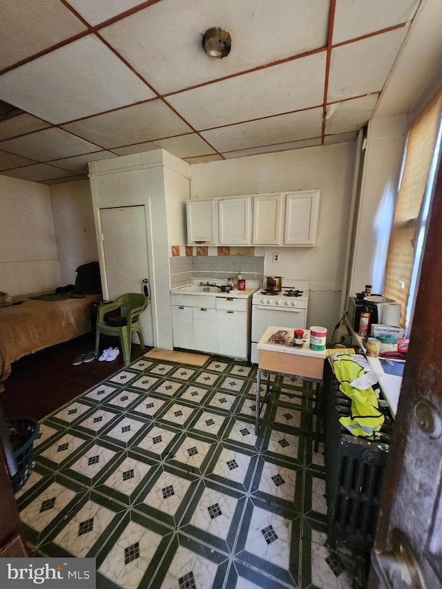 kitchen with decorative backsplash, sink, white cabinetry, and white gas stove