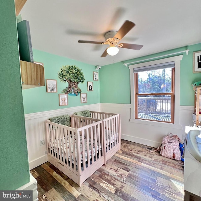 bedroom with hardwood / wood-style flooring, ceiling fan, and a crib