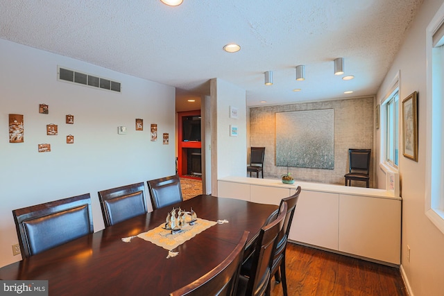 dining space featuring a large fireplace, a textured ceiling, and dark hardwood / wood-style floors