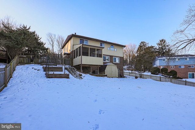 snow covered house featuring a sunroom and a storage unit