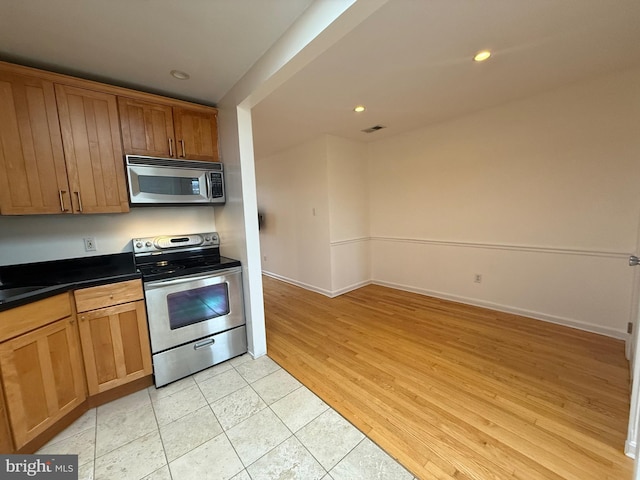 kitchen with stainless steel appliances, brown cabinetry, dark countertops, and visible vents