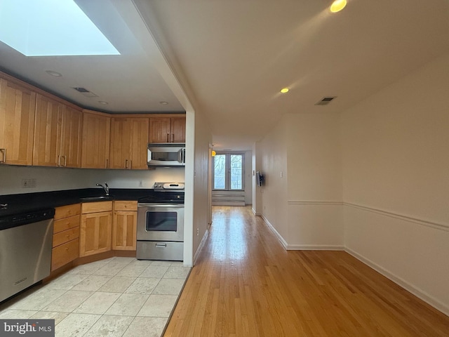 kitchen featuring brown cabinets, stainless steel appliances, dark countertops, visible vents, and a sink