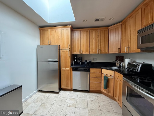 kitchen featuring sink, a skylight, stainless steel appliances, and light tile patterned flooring