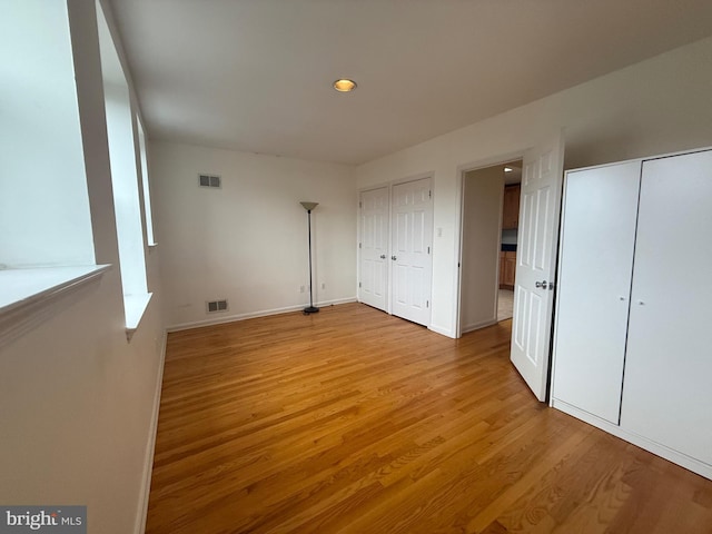 unfurnished bedroom with visible vents, light wood-style flooring, baseboards, and two closets