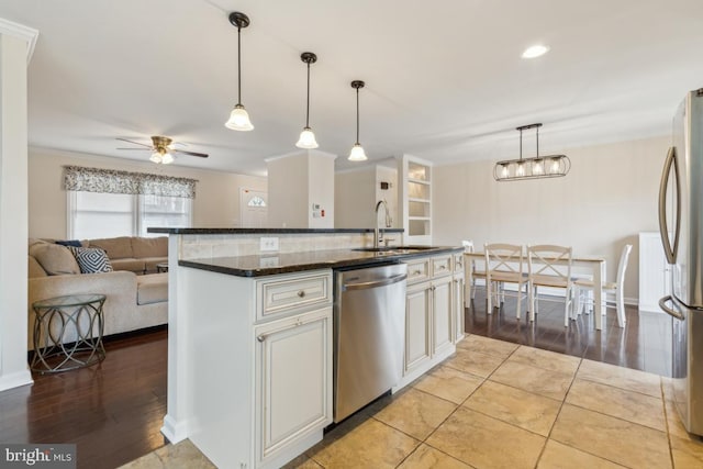 kitchen featuring decorative light fixtures, stainless steel appliances, open floor plan, a sink, and dark stone counters