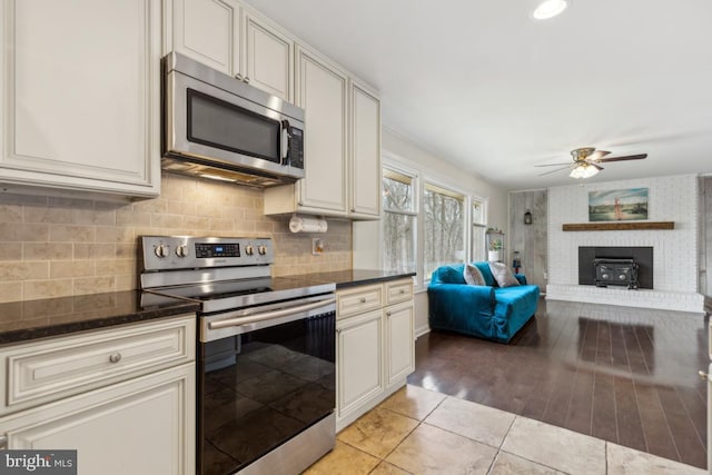 kitchen featuring ceiling fan, stainless steel appliances, open floor plan, backsplash, and dark stone countertops