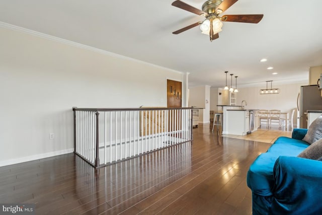 unfurnished living room featuring a sink, baseboards, ornamental molding, and wood finished floors