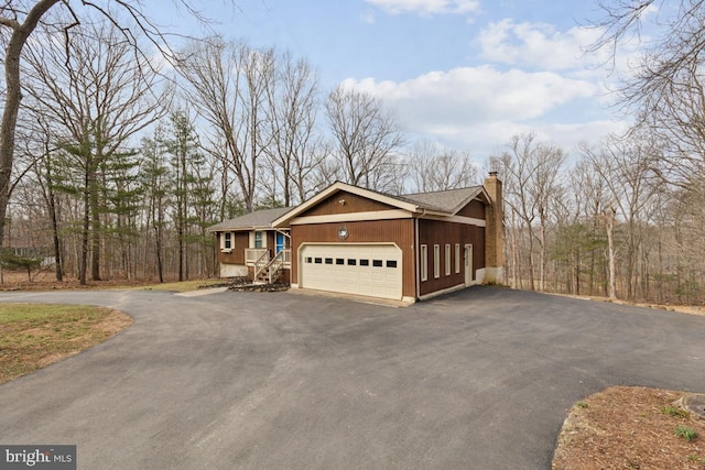 view of side of home with a garage, driveway, a shingled roof, and a chimney