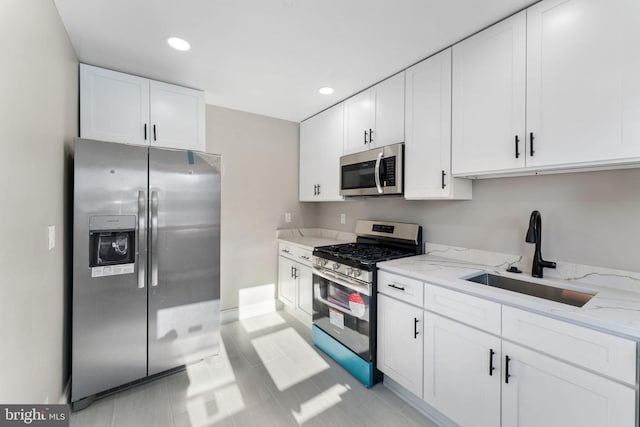 kitchen with stainless steel appliances, sink, white cabinets, light stone counters, and light tile patterned floors