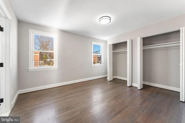 unfurnished bedroom featuring two closets and dark hardwood / wood-style flooring