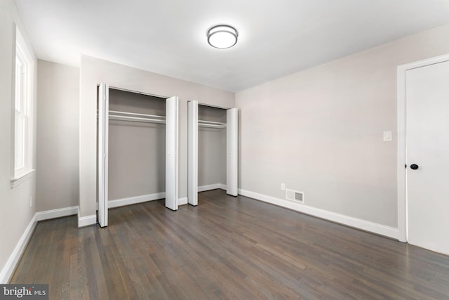 unfurnished bedroom with two closets and dark hardwood / wood-style floors