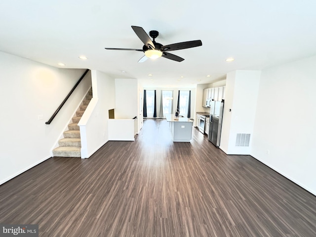 unfurnished living room with ceiling fan, sink, expansive windows, and dark hardwood / wood-style floors