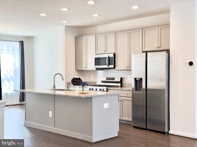 kitchen with light stone countertops, a kitchen island with sink, white cabinets, appliances with stainless steel finishes, and sink