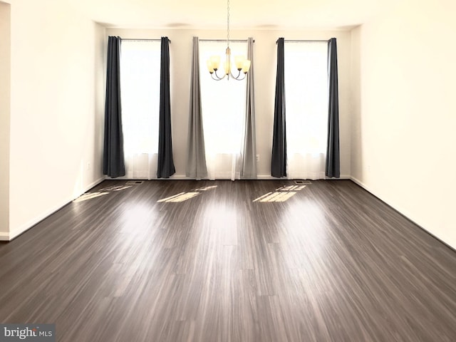 spare room with a healthy amount of sunlight, an inviting chandelier, and dark hardwood / wood-style flooring