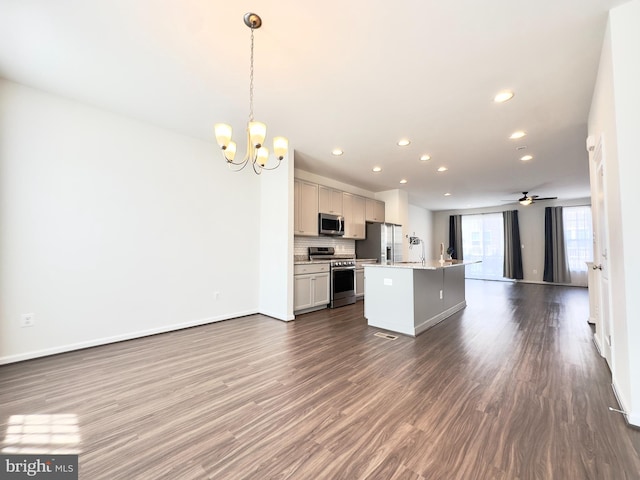 kitchen with appliances with stainless steel finishes, an island with sink, dark hardwood / wood-style flooring, decorative light fixtures, and ceiling fan with notable chandelier