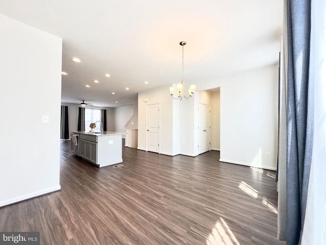 interior space featuring sink, decorative light fixtures, ceiling fan with notable chandelier, dark hardwood / wood-style floors, and a center island with sink