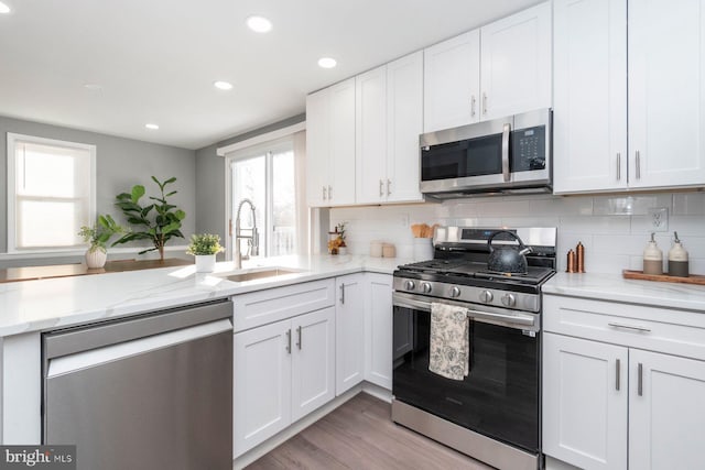 kitchen featuring stainless steel appliances, decorative backsplash, white cabinets, light hardwood / wood-style flooring, and sink