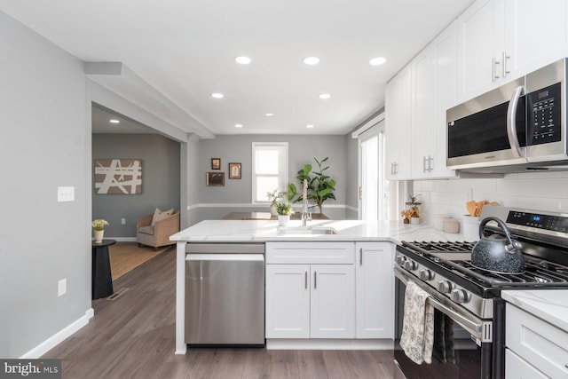 kitchen with white cabinets, stainless steel appliances, dark hardwood / wood-style floors, and kitchen peninsula