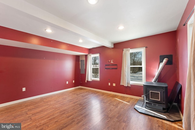 unfurnished living room with beamed ceiling, wood finished floors, a wood stove, and baseboards