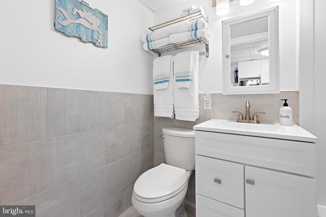 bathroom with toilet, tile walls, and vanity