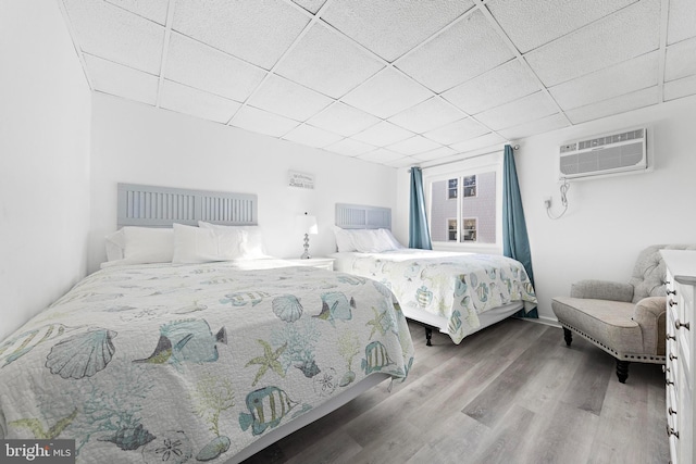 bedroom featuring a paneled ceiling, hardwood / wood-style flooring, and a wall mounted air conditioner