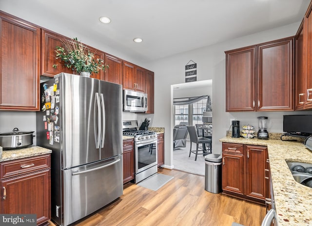 kitchen with sink, light hardwood / wood-style floors, light stone counters, and appliances with stainless steel finishes