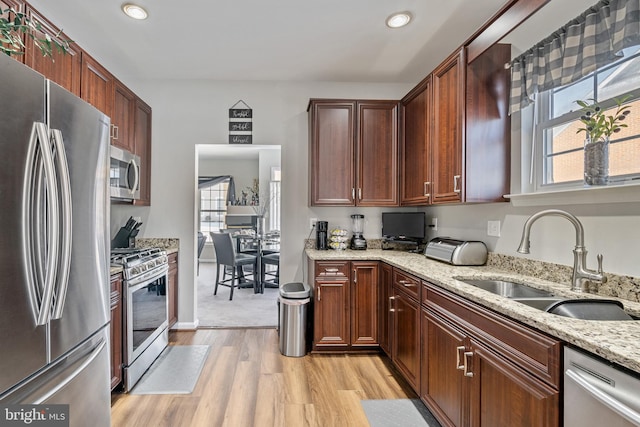 kitchen with light stone counters, appliances with stainless steel finishes, light hardwood / wood-style floors, and sink