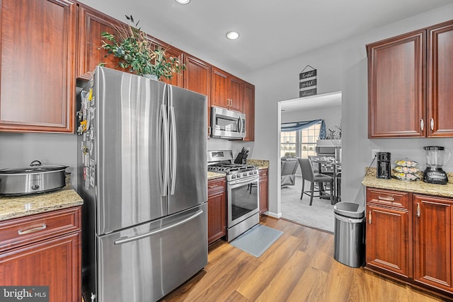 kitchen with stainless steel appliances, light stone countertops, and light hardwood / wood-style flooring