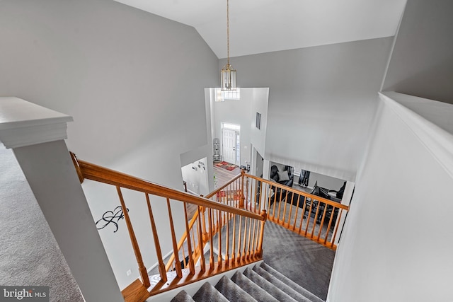 staircase featuring an inviting chandelier, vaulted ceiling, and carpet floors