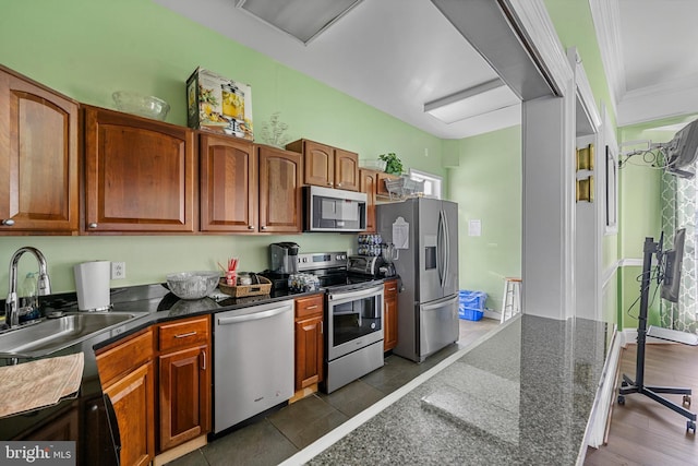 kitchen with stainless steel appliances, sink, ornamental molding, dark stone counters, and dark tile patterned floors