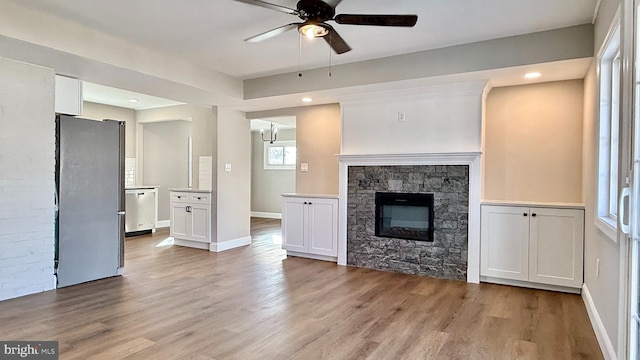 unfurnished living room with ceiling fan, light hardwood / wood-style flooring, and a stone fireplace