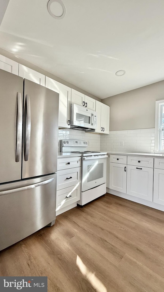 kitchen featuring white appliances, light hardwood / wood-style floors, white cabinets, and decorative backsplash