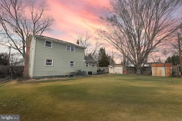 back house at dusk featuring a yard and a storage unit