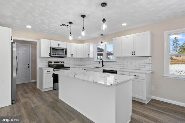 kitchen with sink, white cabinetry, light stone countertops, a kitchen island, and appliances with stainless steel finishes