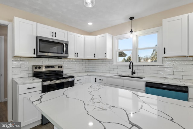 kitchen featuring light stone counters, decorative light fixtures, white cabinets, appliances with stainless steel finishes, and sink