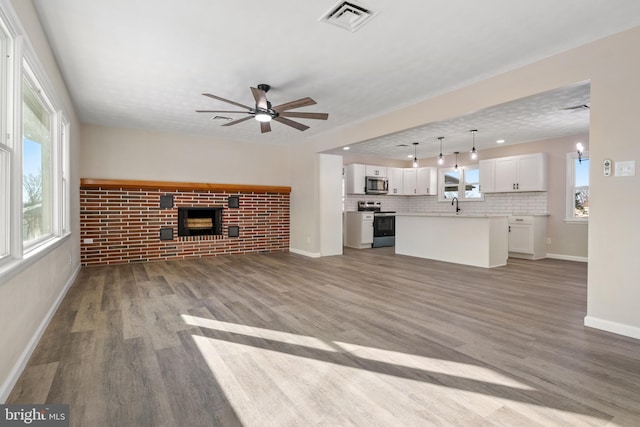 unfurnished living room with a textured ceiling, brick wall, a fireplace, ceiling fan, and wood-type flooring