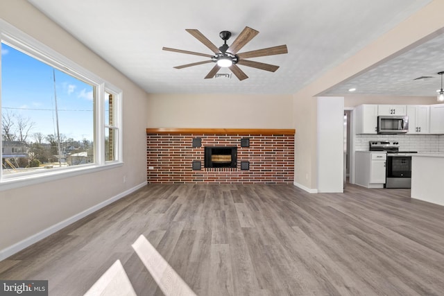 unfurnished living room with a brick fireplace, light wood-type flooring, and ceiling fan