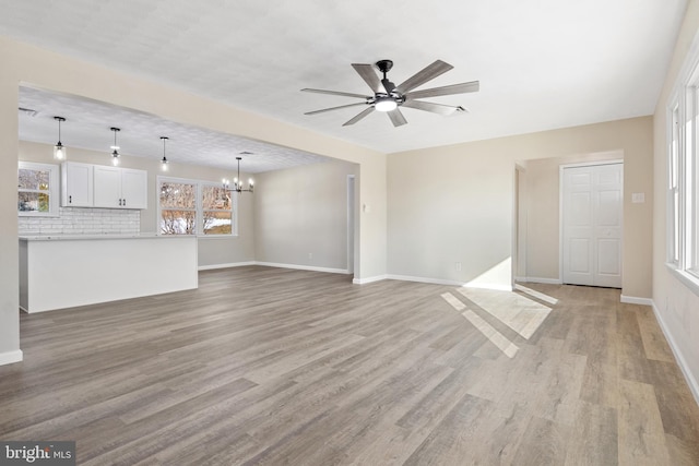 unfurnished living room with ceiling fan with notable chandelier and light hardwood / wood-style flooring