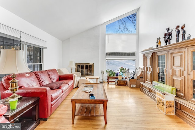 living room featuring high vaulted ceiling, a large fireplace, and light hardwood / wood-style flooring