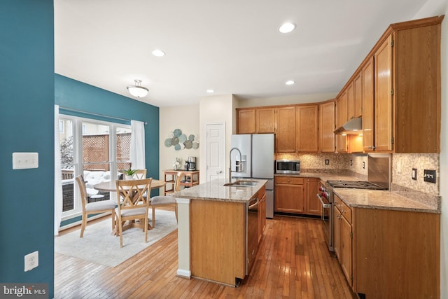 kitchen featuring light wood-type flooring, a kitchen island with sink, appliances with stainless steel finishes, and light stone counters