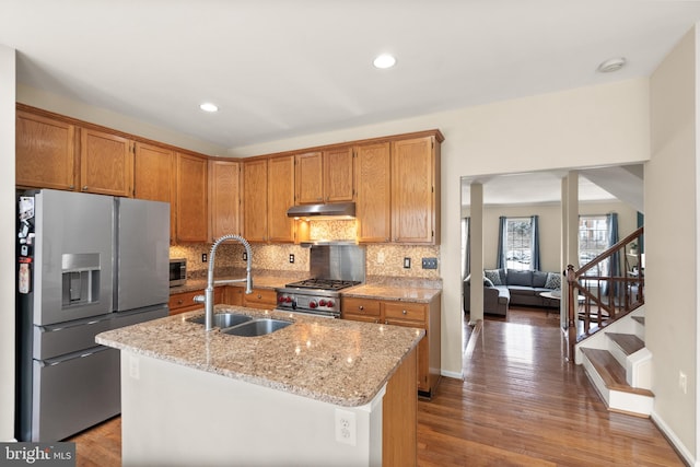 kitchen with stainless steel appliances, a kitchen island with sink, light stone counters, and sink