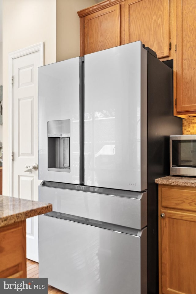 kitchen featuring decorative backsplash, light stone counters, and fridge with ice dispenser