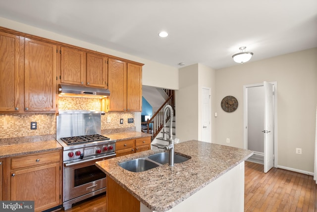 kitchen featuring premium range, sink, light hardwood / wood-style flooring, an island with sink, and light stone counters