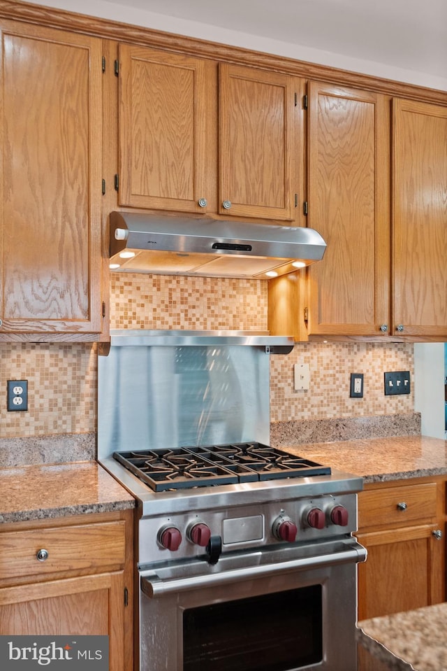 kitchen with light stone countertops, decorative backsplash, and high end stove