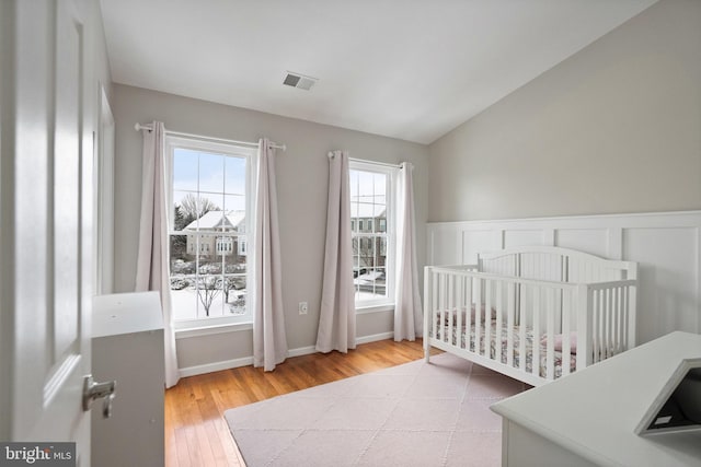 bedroom with lofted ceiling, a nursery area, and light hardwood / wood-style floors